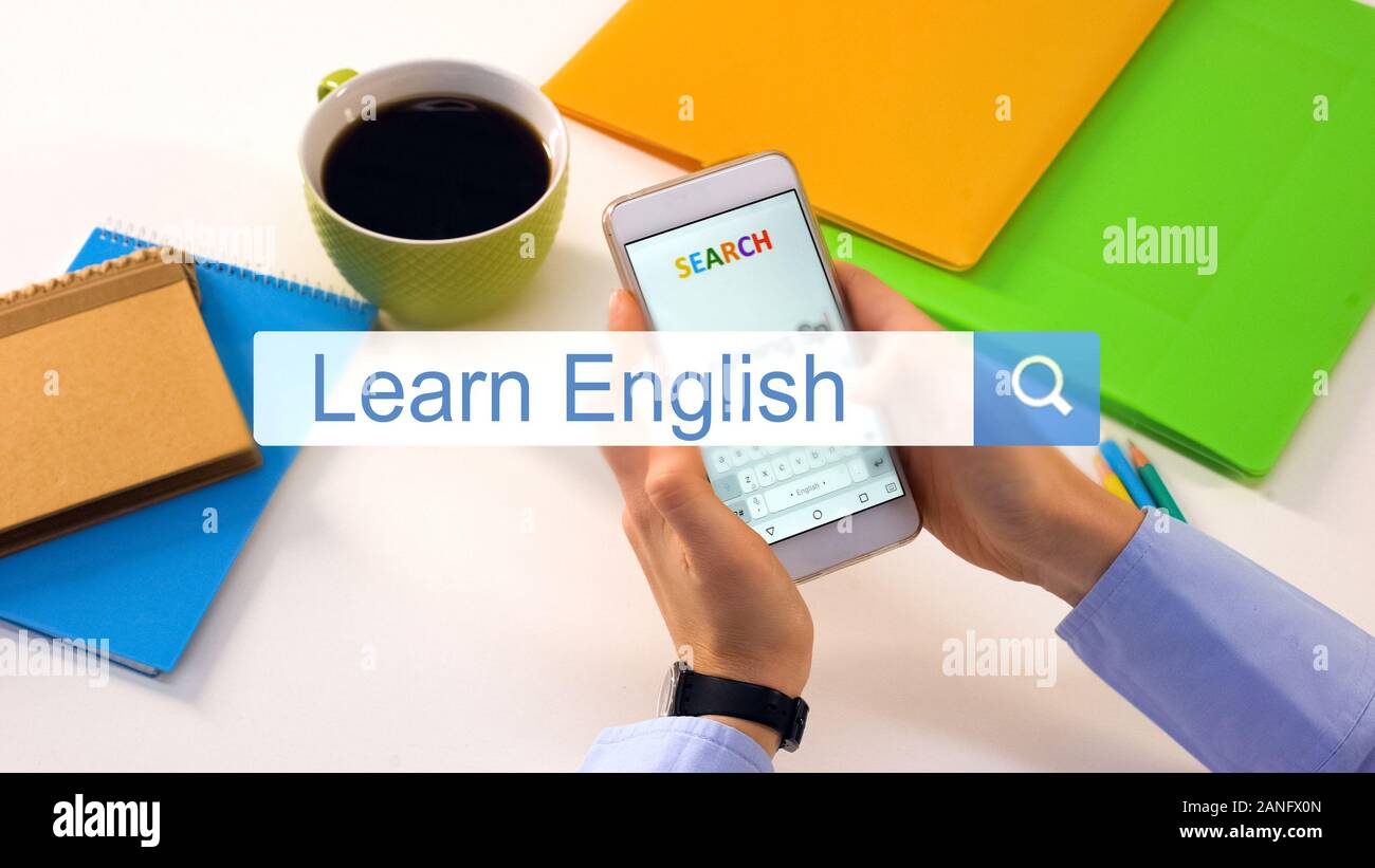 Person inserting learn English phrase on smartphone search bar, education Stock Photo