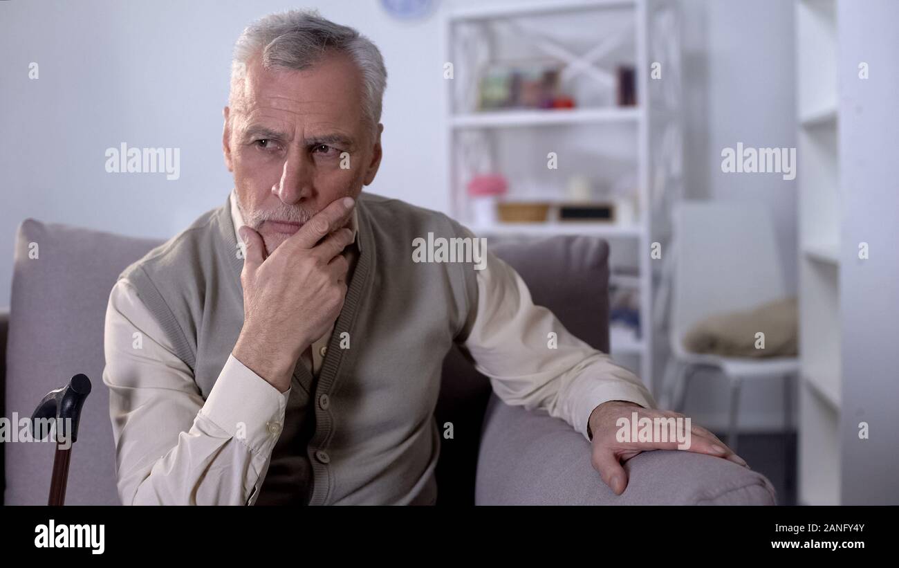 Upset old man sitting on couch, thinking over health problems, low pensions Stock Photo