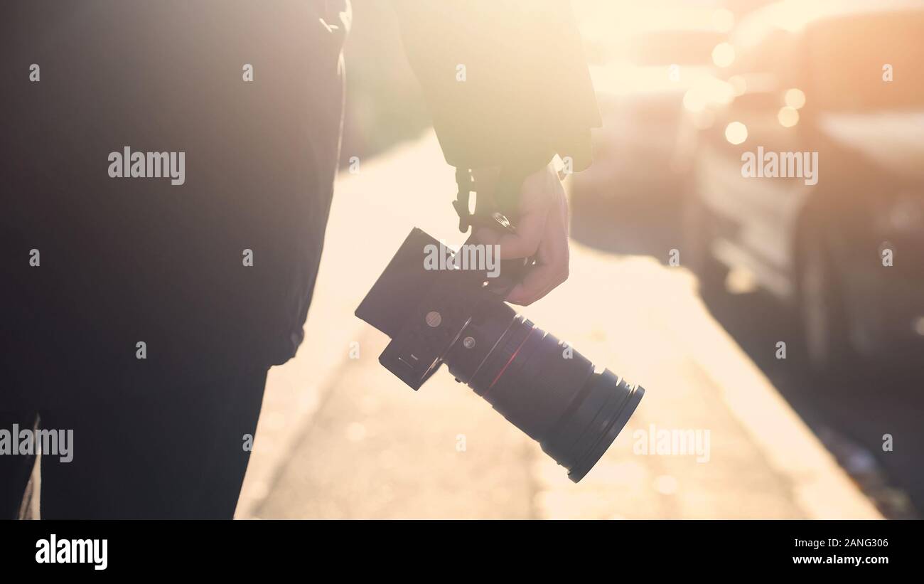 Professional photojournalist holding camera, walking on street, paparazzi spying Stock Photo