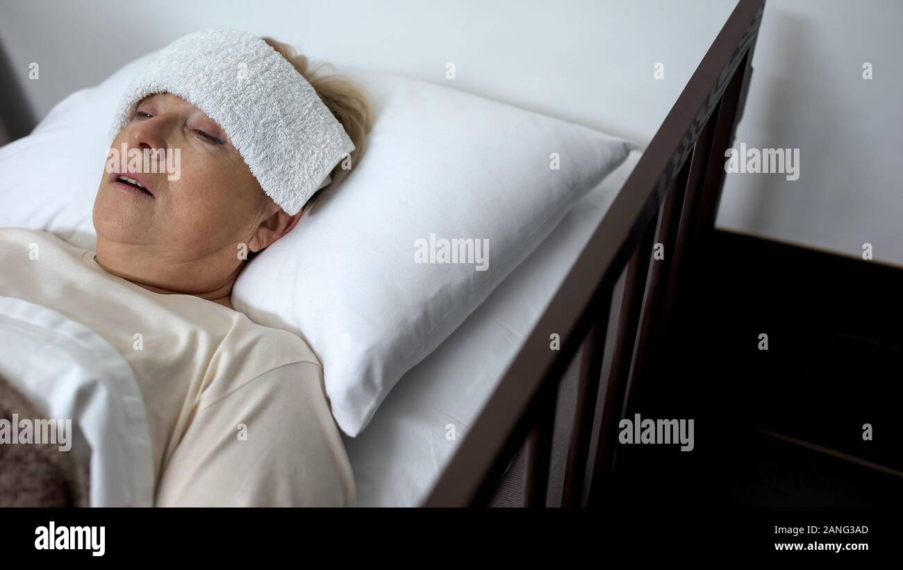 Sick mature woman lying in hospital bed with compress on forehead
