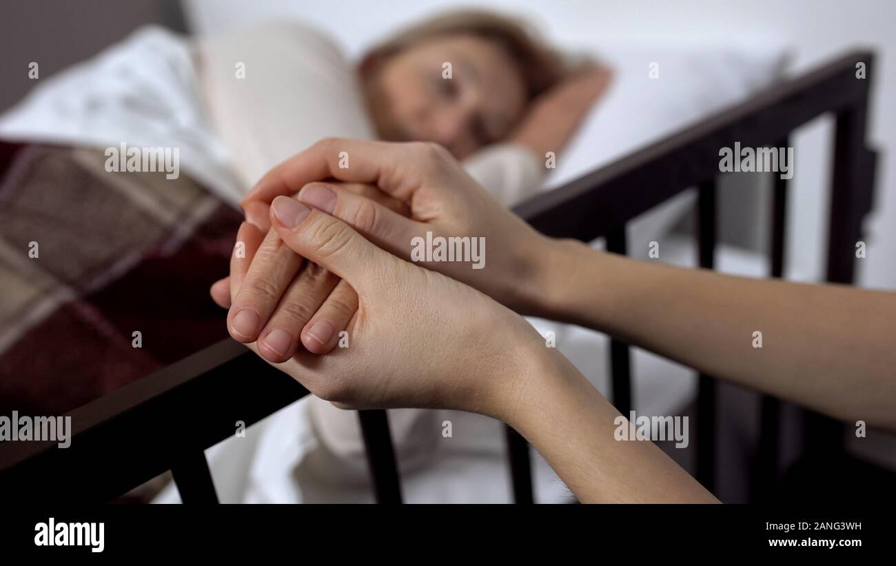 Daughter supporting her terminally ill mother lying on hospital bed, hospice Stock Photo