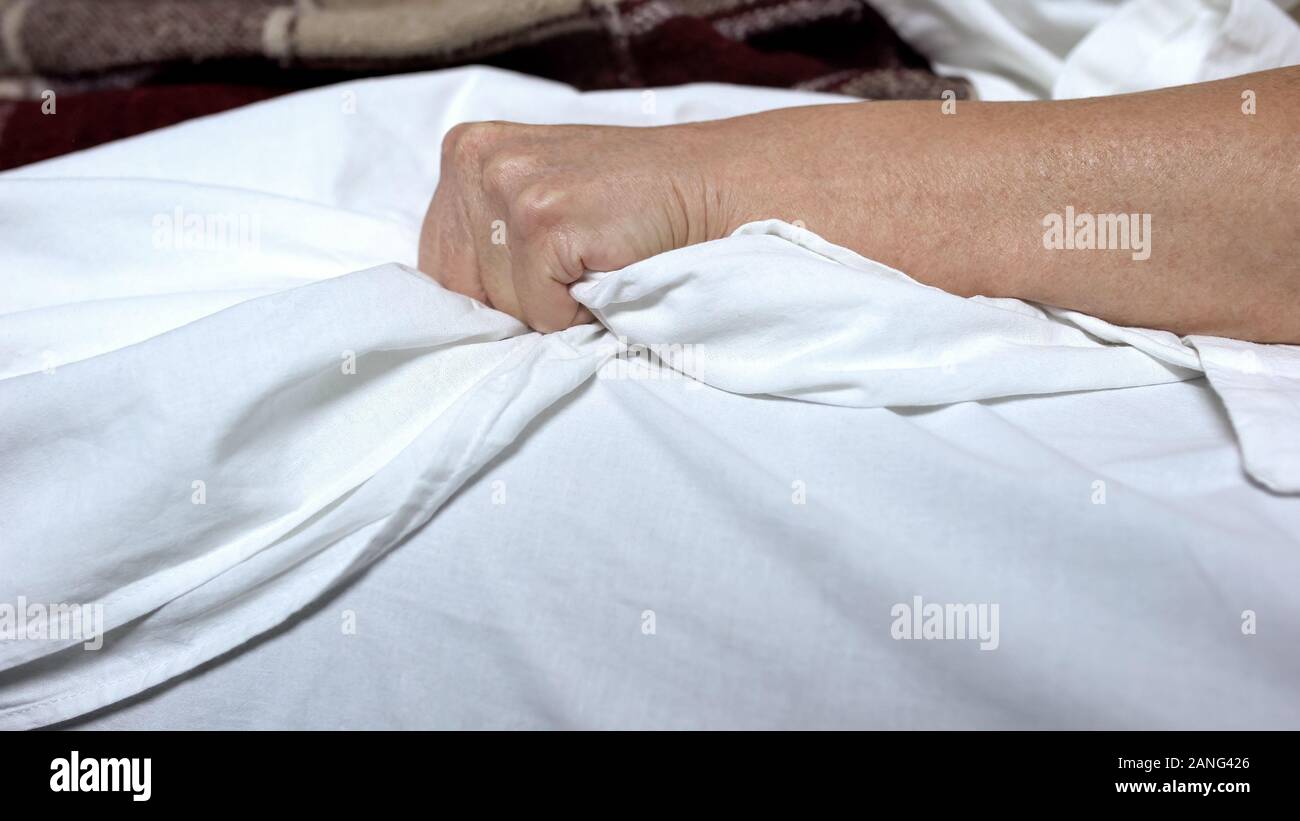 Terminally-ill woman clenching bedsheets feeling terrible pain, death convulsion Stock Photo