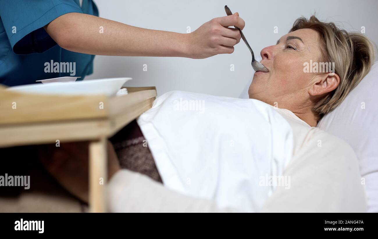 Nurse feeding disabled mature woman with porridge, care for patients, hospice Stock Photo