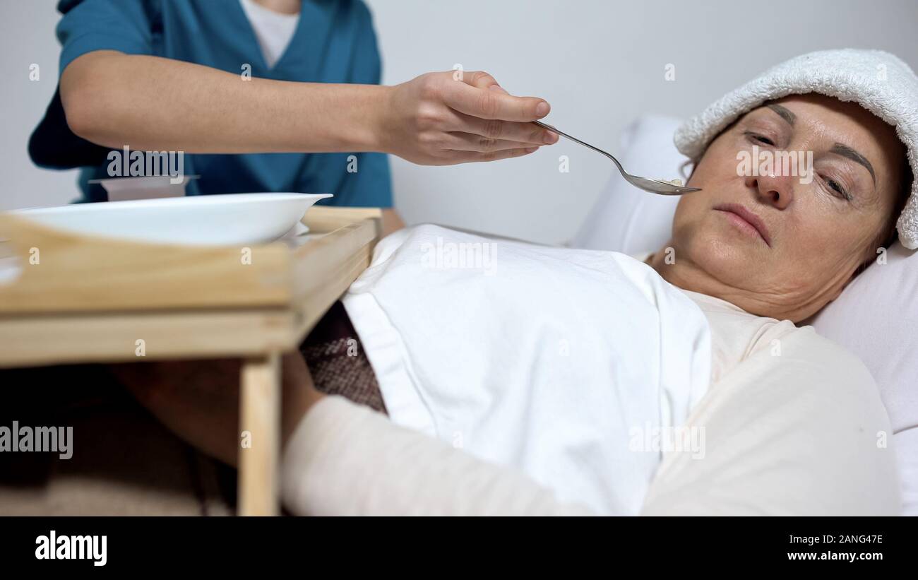 Terminally ill woman with compress on forehead refusing from hospice porridge Stock Photo