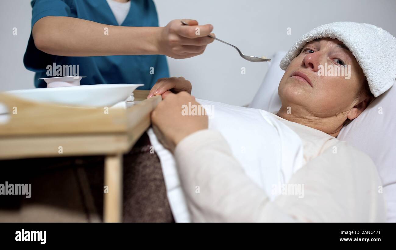 Terminally ill woman looking at camera, nurse feeding patient