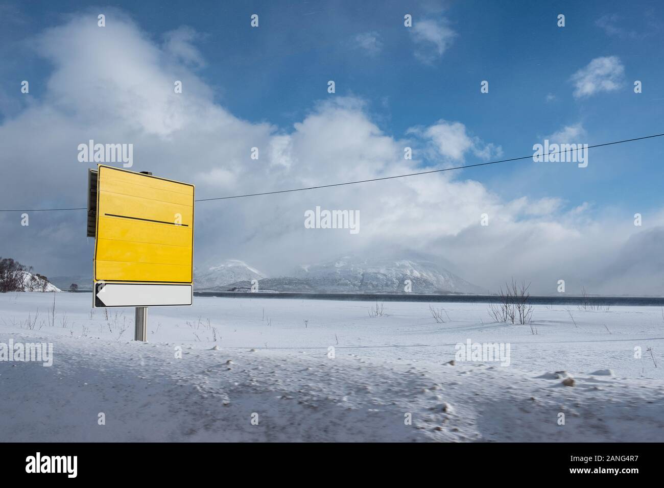 Yellow traffic signboard on snow covered roadside at coastline Stock Photo