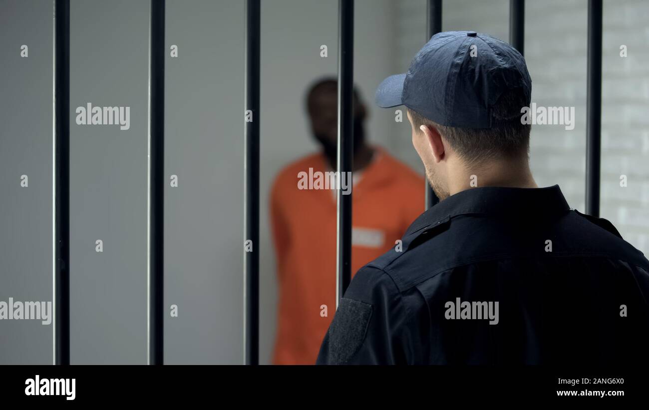 Warden looking at dangerous criminal standing in cell, life sentence, prison Stock Photo