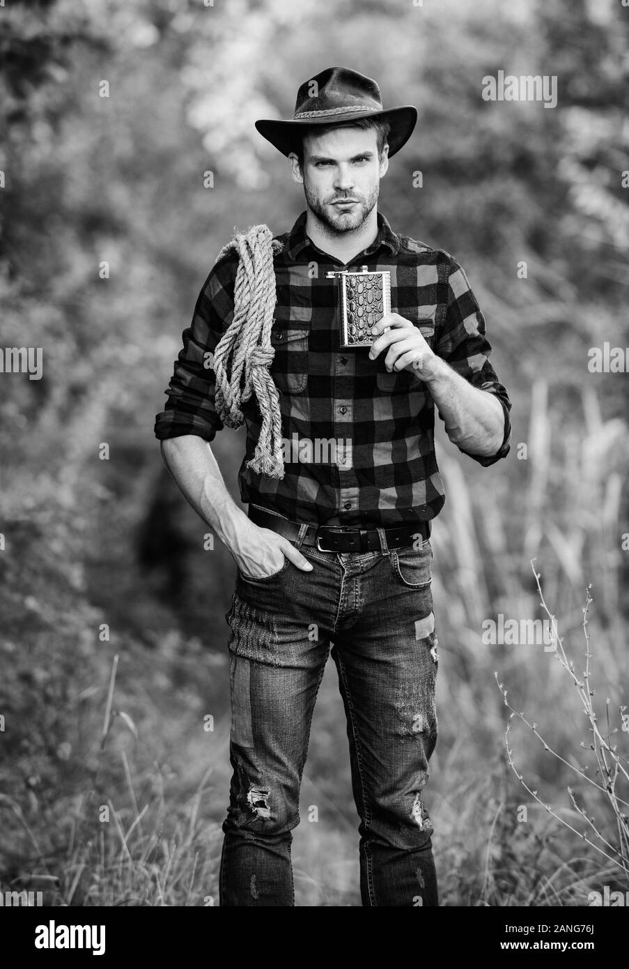 Cowboy ranch worker. Bourbon whiskey. Western culture. Man wearing hat hold rope and flask. Lasso tool American cowboy. Brutal cowboy drinking alcohol Stock Photo