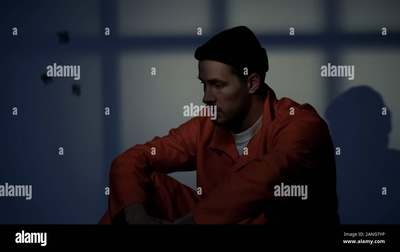 Depressed prisoner sitting alone in dark cell, feeling guilty about ...