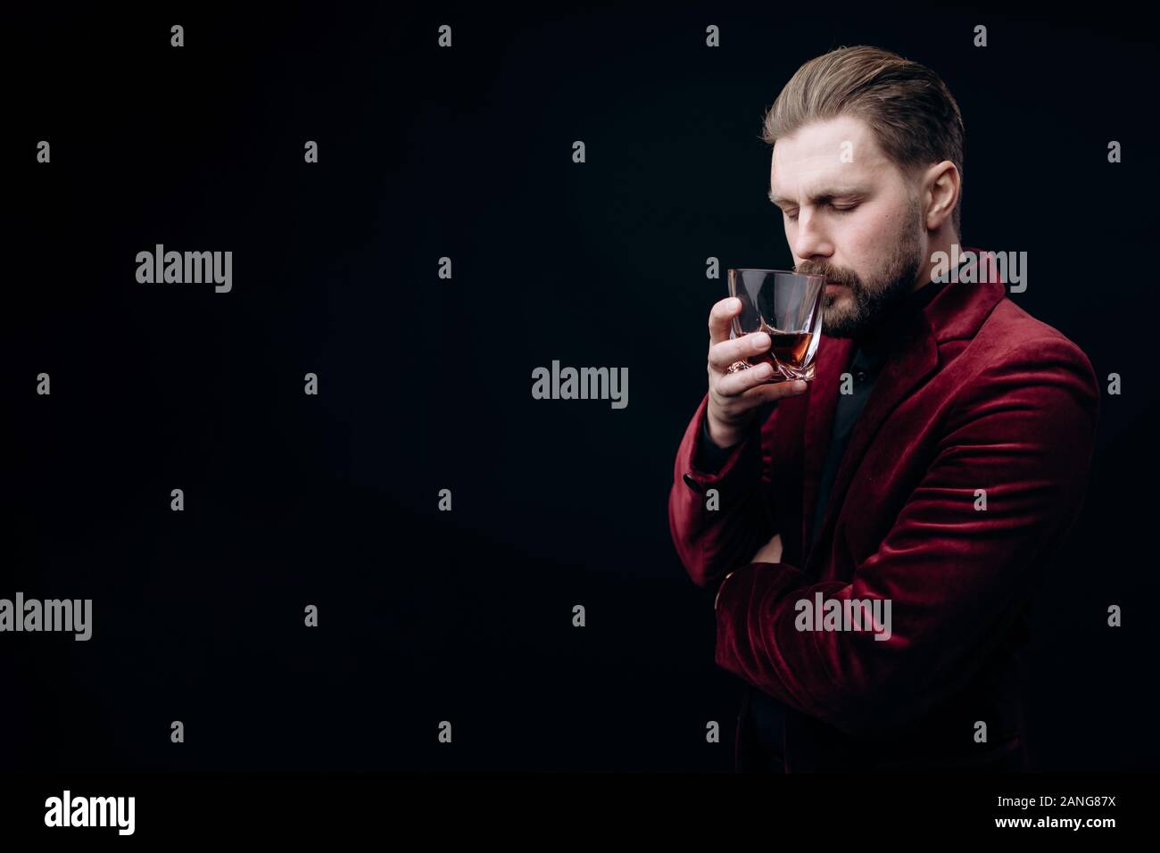 Bearded Brown-haired Man in Velvet Jacket Smelling Whiskey Stock Photo