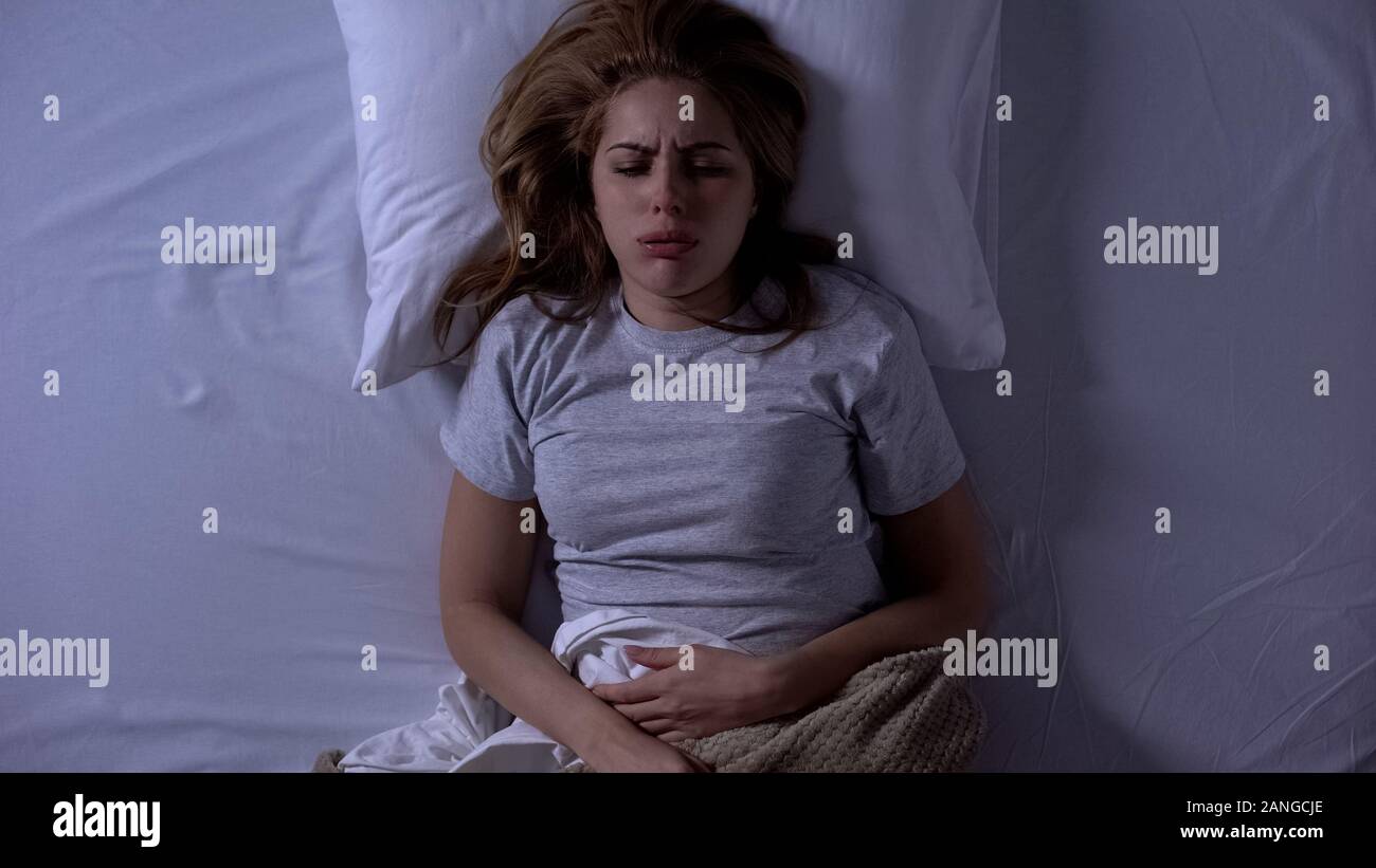 Lady feeling sharp lower abdominal pain during sleeping, suffering from cystitis Stock Photo