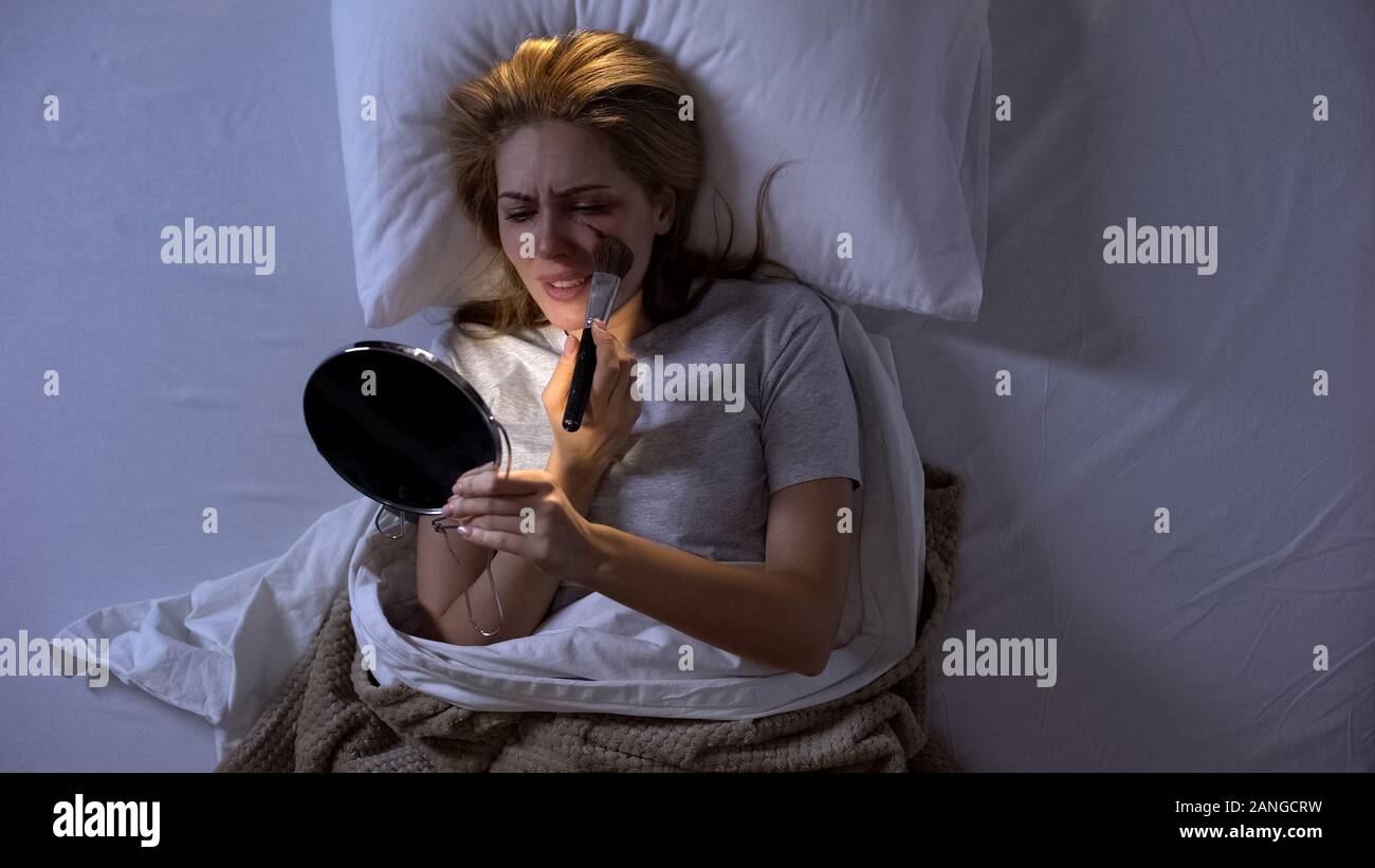 Crying female victim trying to cover wound on face with powder