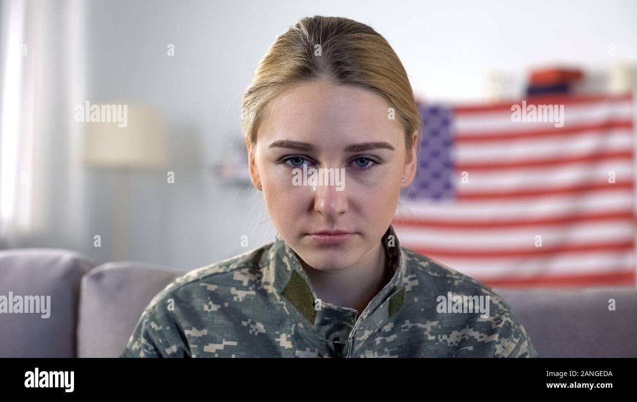 Crying american female soldier looking at camera against US national flag, PTSD Stock Photo
