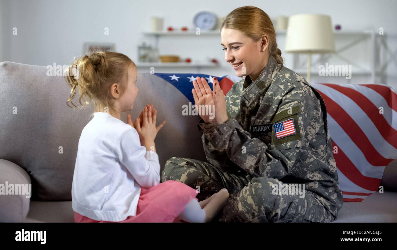 Happy american female soldier and child playing hands on sofa, family time, fun Stock Photo