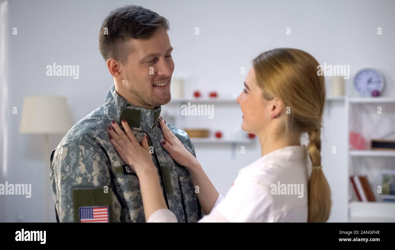 Caring female adjusting uniform of US soldier boyfriend, admiring beloved man Stock Photo