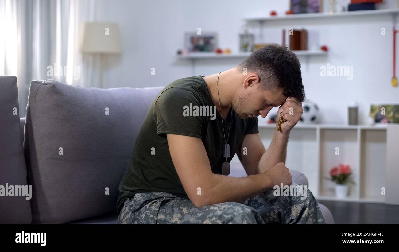 Male military praying, holding wooden cross in hand, remembering dead comrade Stock Photo