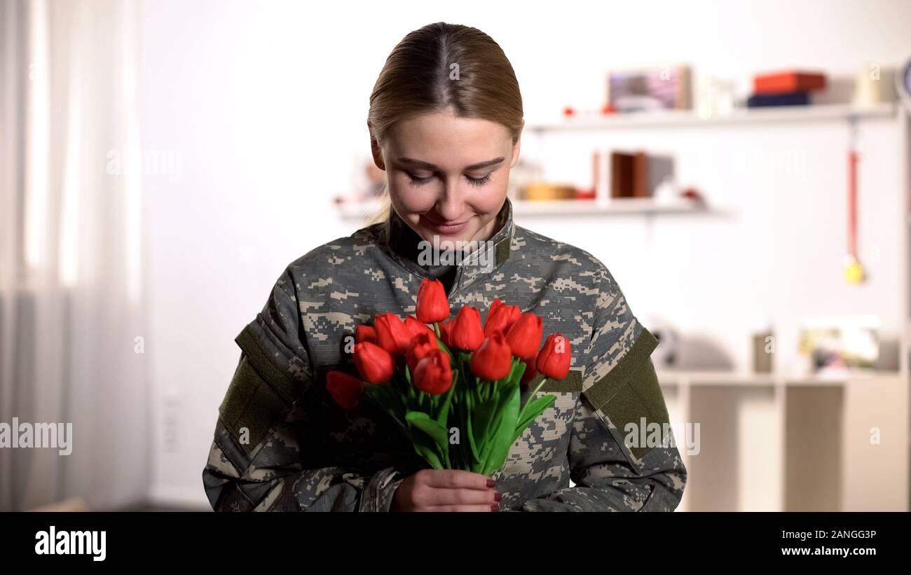Happy female soldier in uniform sniffing aroma of tulips bouquet and smiling Stock Photo