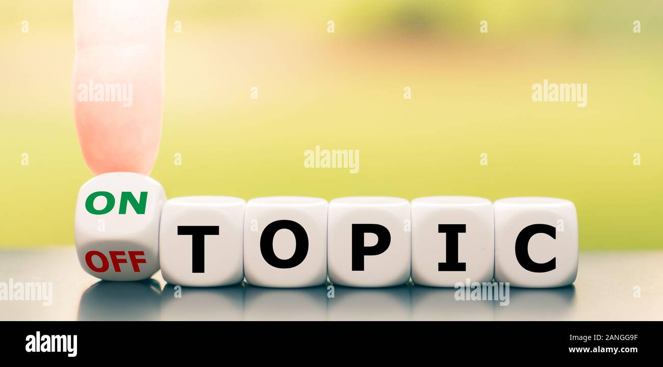Hand turns a dice and changes the expression 'off topic' to 'on topic'. Stock Photo