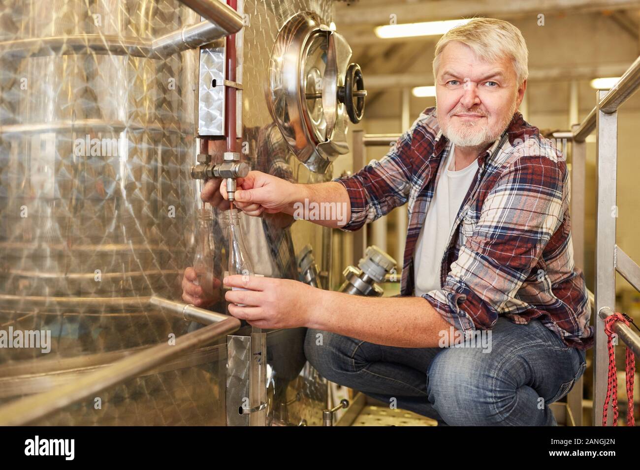 Man as a winemaker in a winery checks fresh wine at the fermentation tank Stock Photo
