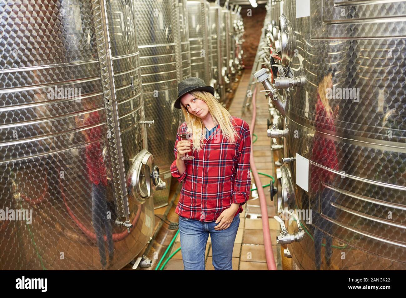 Young woman as a winemaker in front of fermentation tank in the winery with a glass of red wine Stock Photo