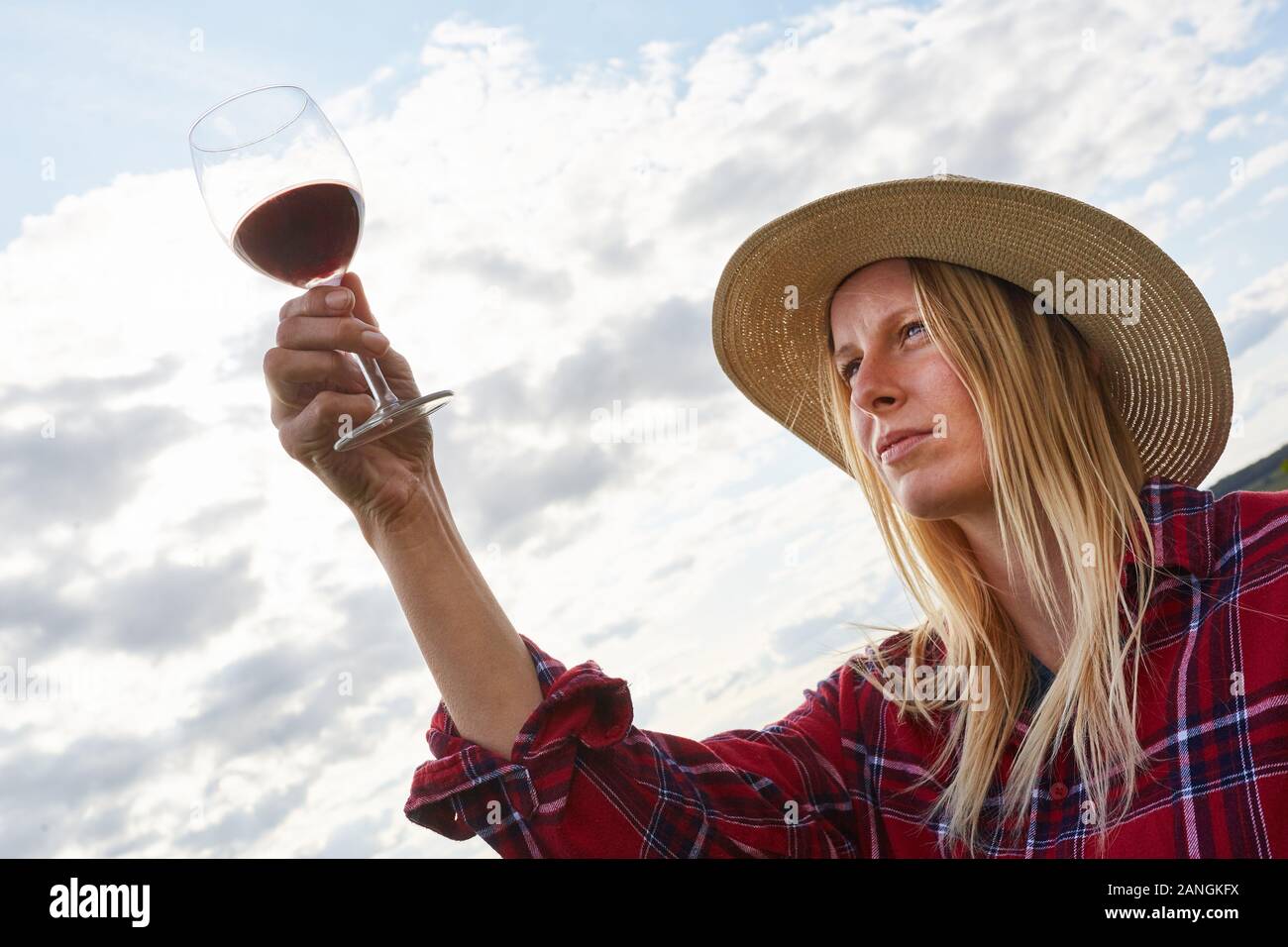 Young woman as a winemaker takes a critical look at a glass of red wine ...