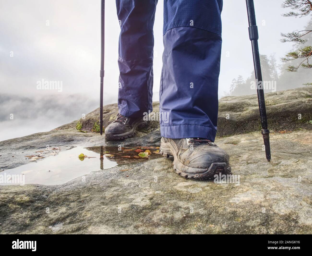 Woman legs in high waterproof boots make step over water pool on the rocky journey. Misty rainy weather in mountains Stock Photo