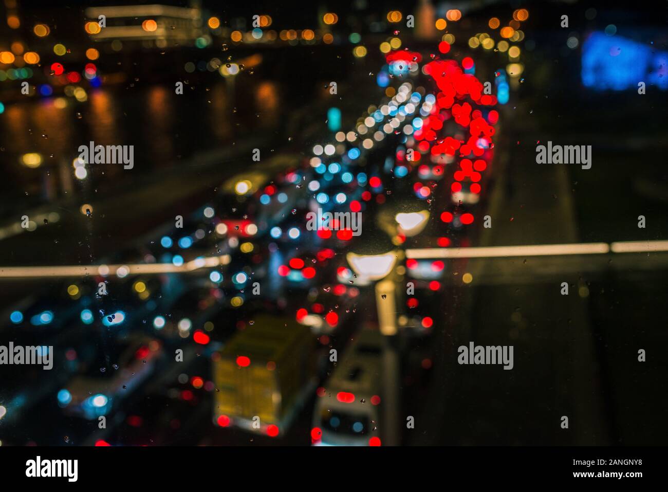 Night road with blurry cars and headlights. Car traffic shot through glass, focusing on raindrops. Rainy and cloudy day Stock Photo