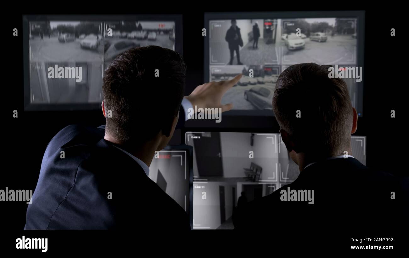 Private agents monitoring CCTV footage, searching for criminal, discussion Stock Photo