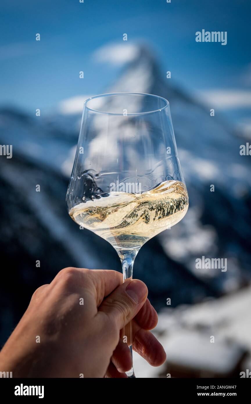 hand holding a glass of white wine in front of Matterhorn in winter in a Restaurant Stock Photo