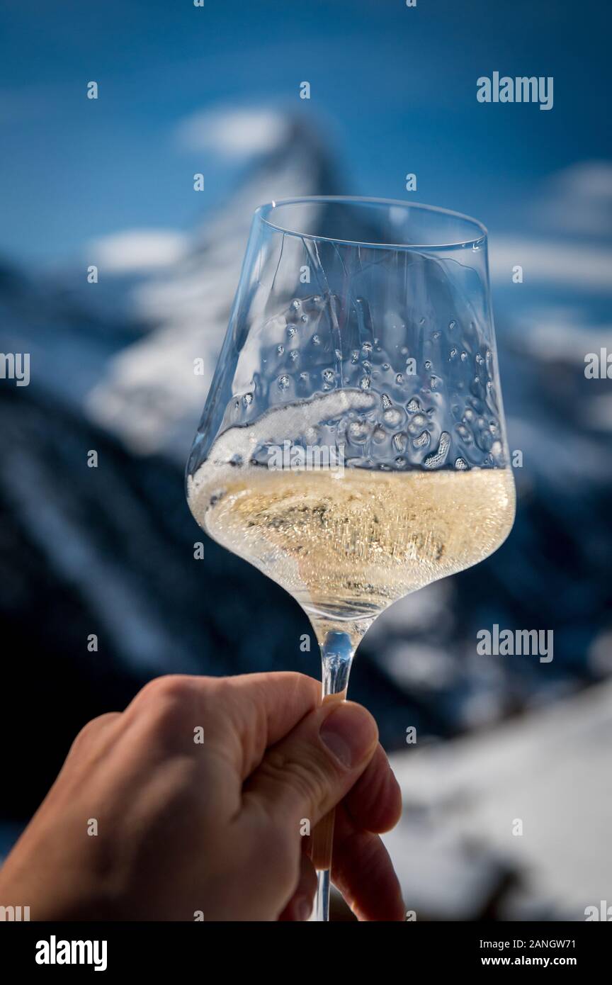 hand swinging a glass of white wine in front of Matterhorn in winter in a Restaurant Stock Photo