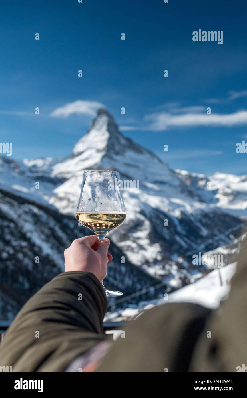hand holding a glass of white wine in front of Matterhorn in winter in a Restaurant Stock Photo