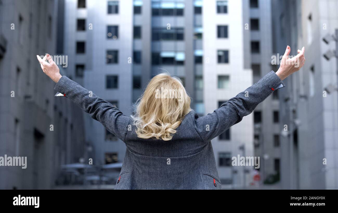 Carefree blond woman in formal suit raised up hands back view, female wellness Stock Photo