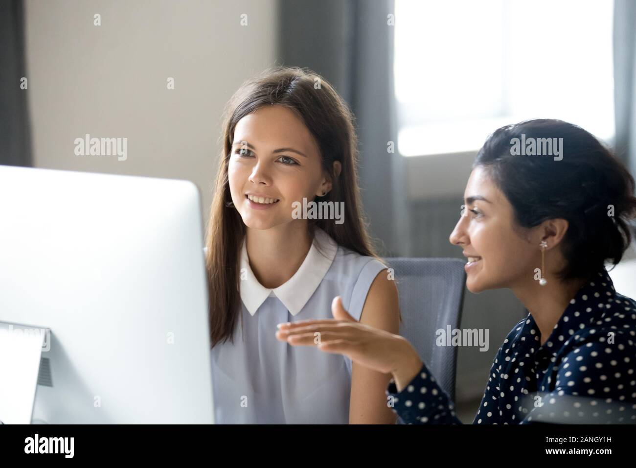 Smiling multiracial millennial women work on computer in office ...