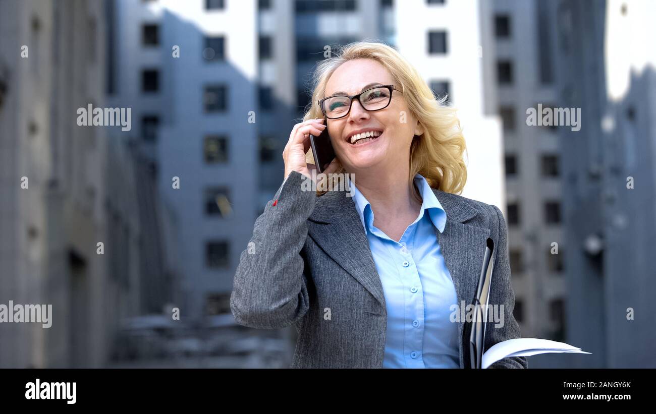 Successful business lady with documents in hand talking phone and smiling, work Stock Photo