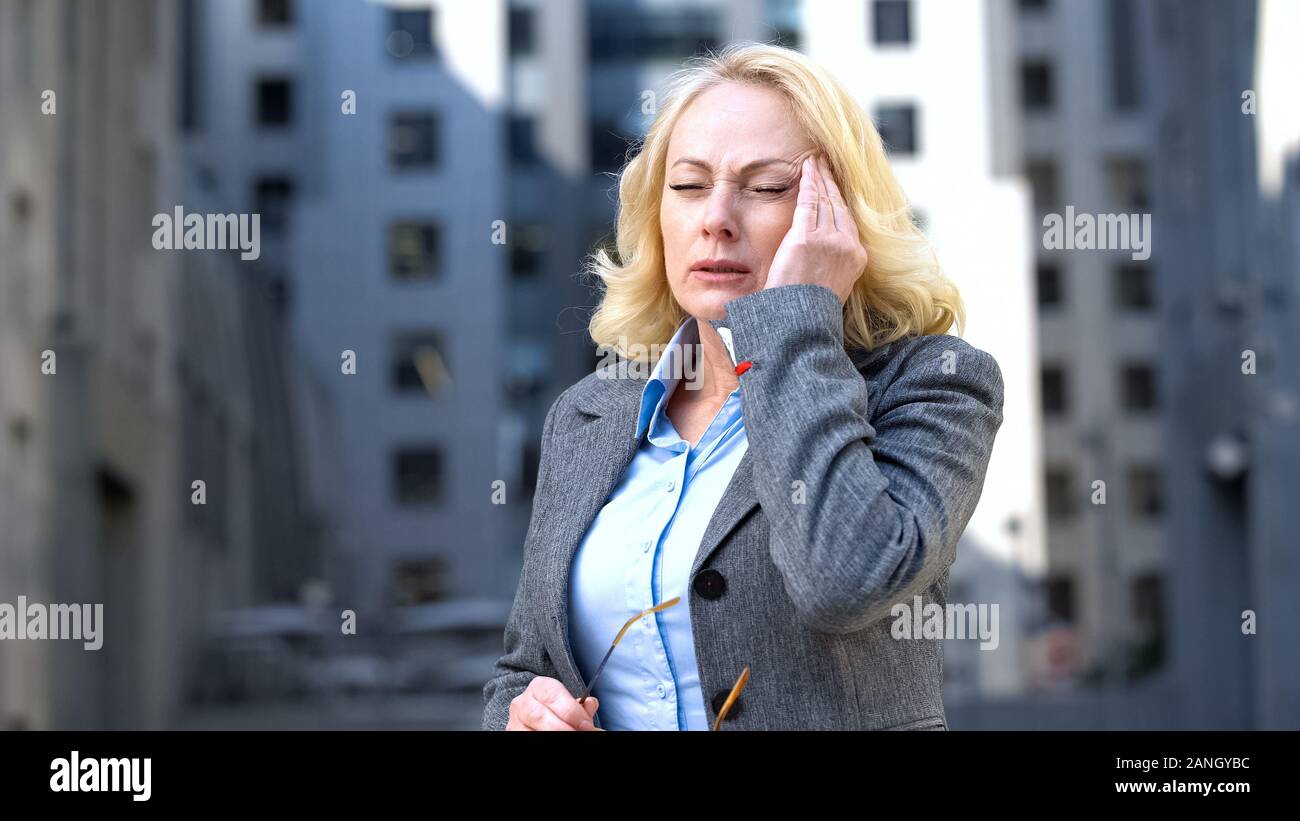 Sick aged lady in suit suffering migraine, work pressure, busy lifestyle tension Stock Photo