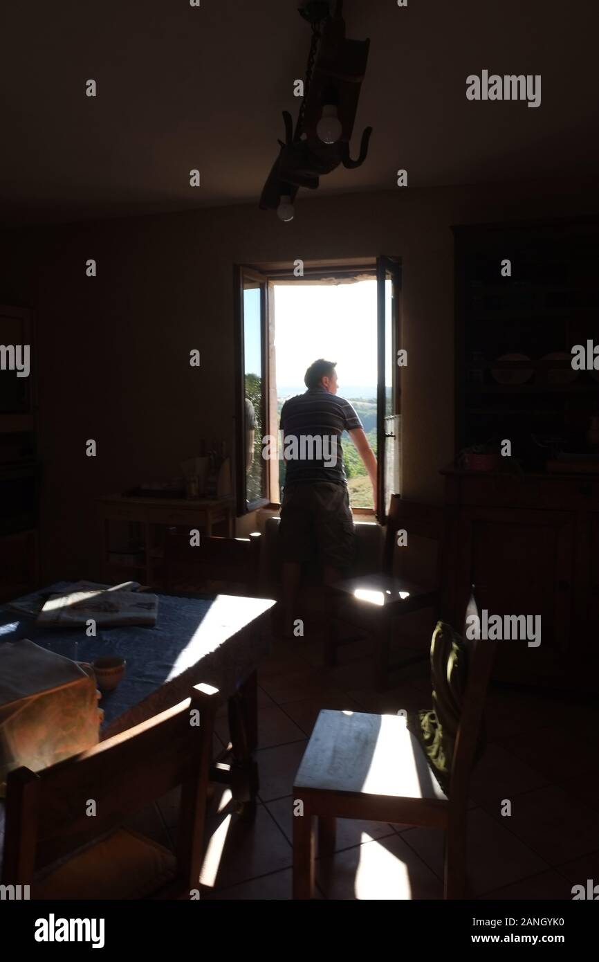 Man stood at a window looking outside Stock Photo