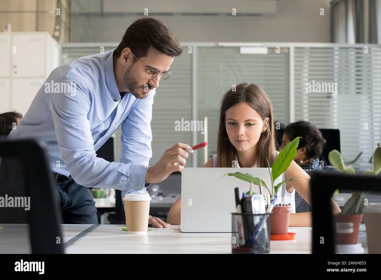 Serious male manager in glasses teach young female intern working at laptop, explain issues pointing, man trainer or coach instruct girl trainee helpi Stock Photo