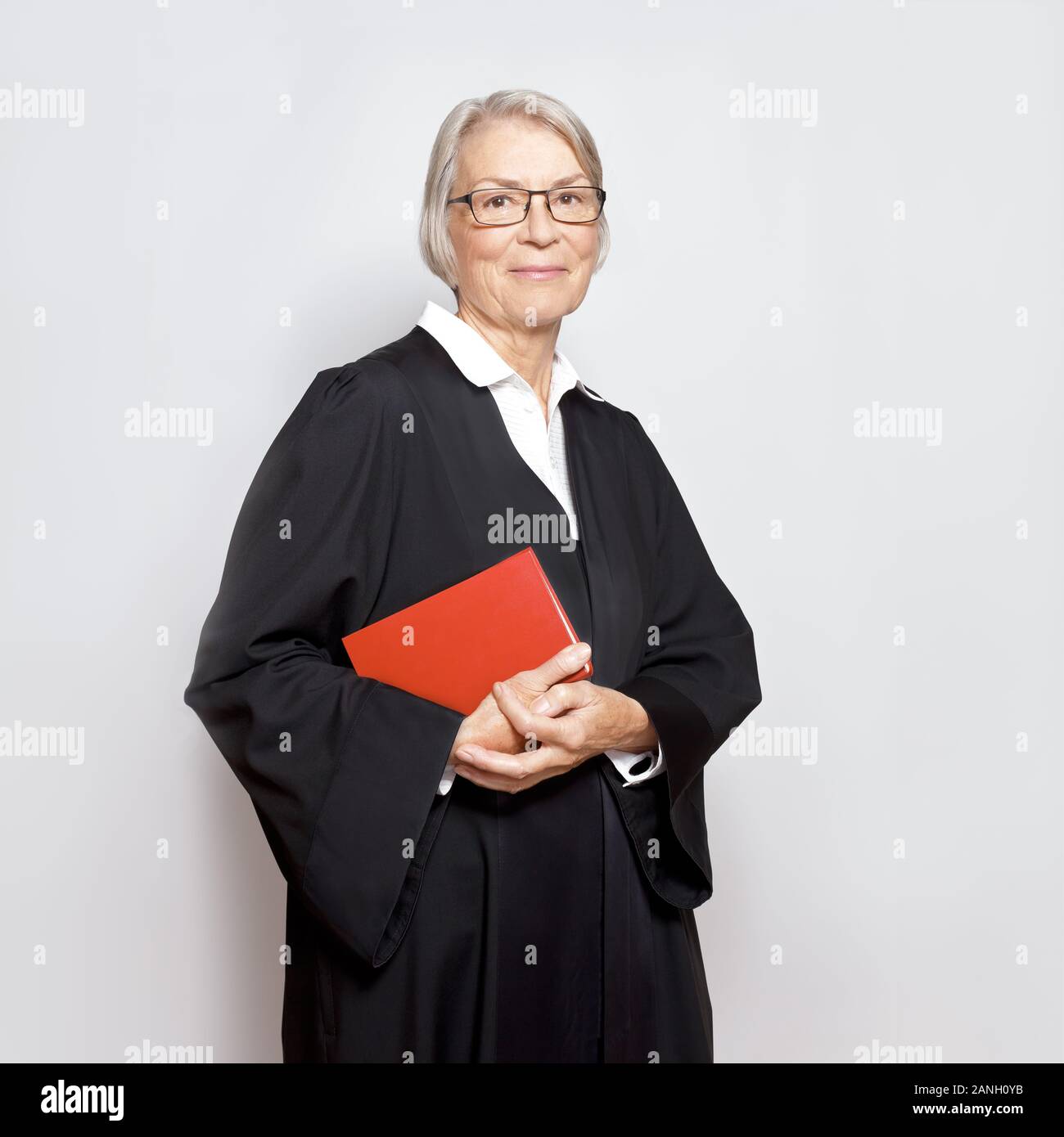 Best legal advice concept: portrait of a friendly smiling mature woman with law book in a black judge's gown. Stock Photo