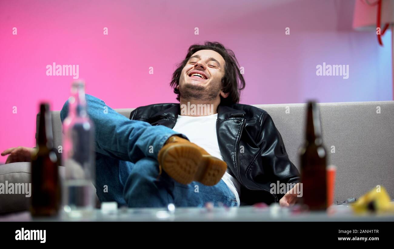Relaxed drunk young man sitting on sofa, boozer enjoying music at dance party Stock Photo