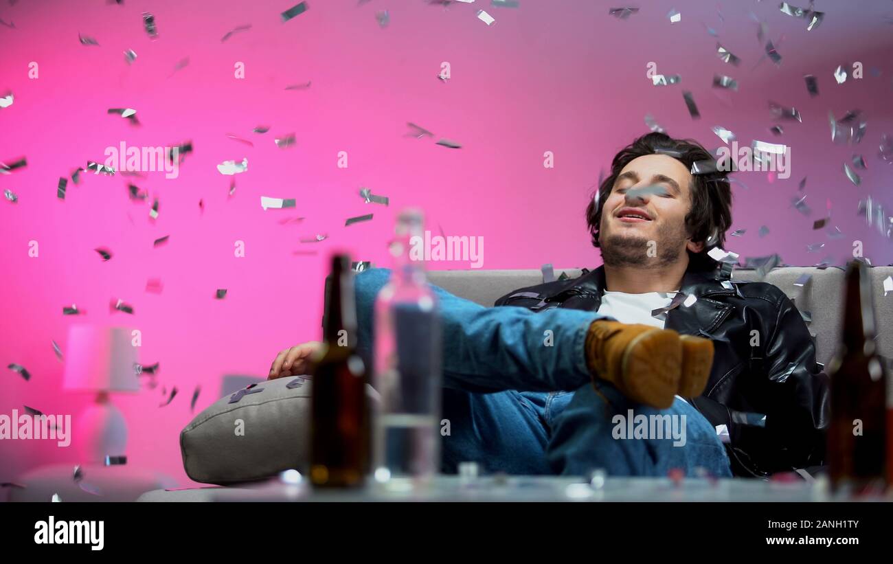 Happy drunk guy chilling out on couch at party, confetti falling down, relax Stock Photo