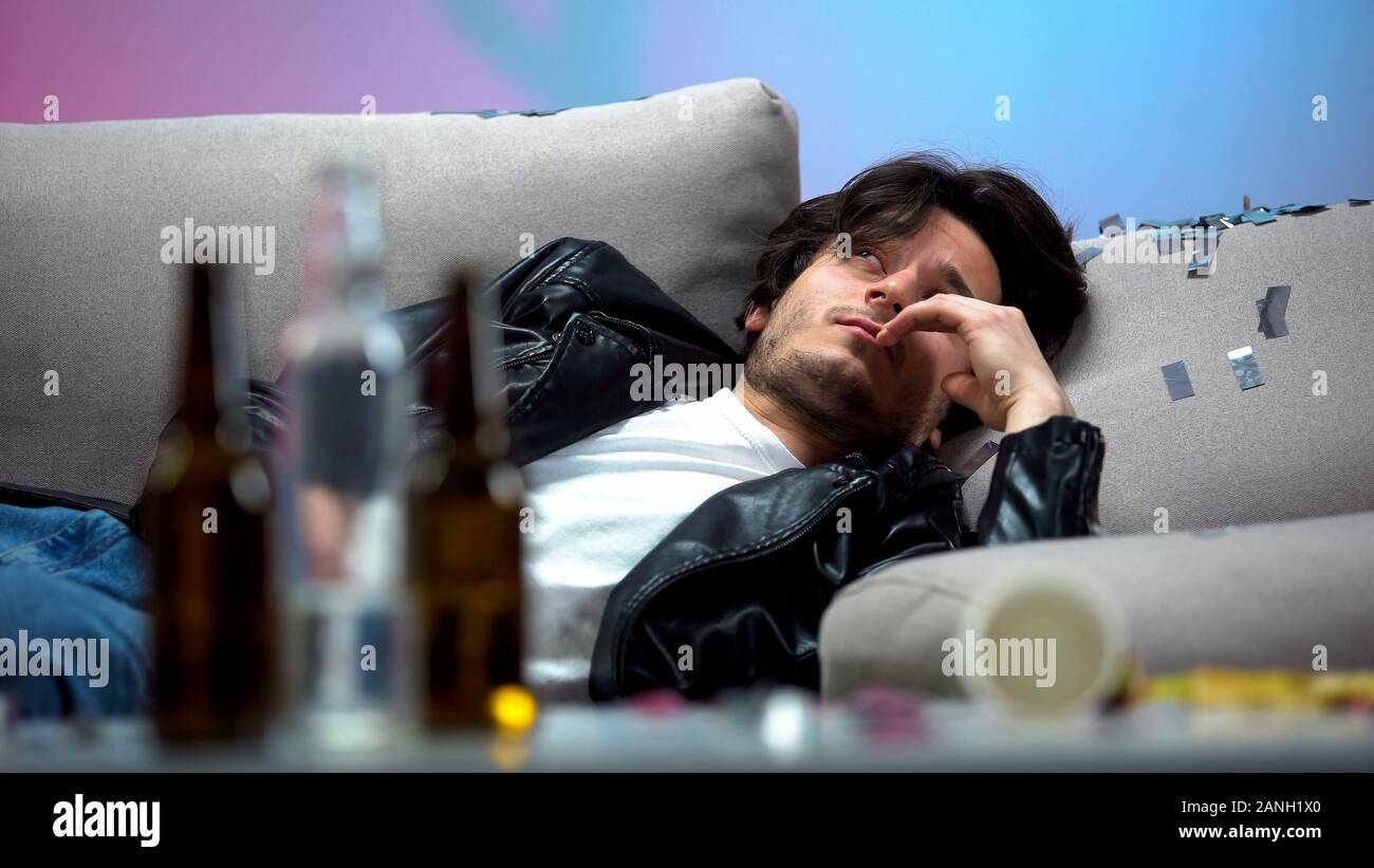 Intoxicated young man waking up on messy couch after party, looking around Stock Photo