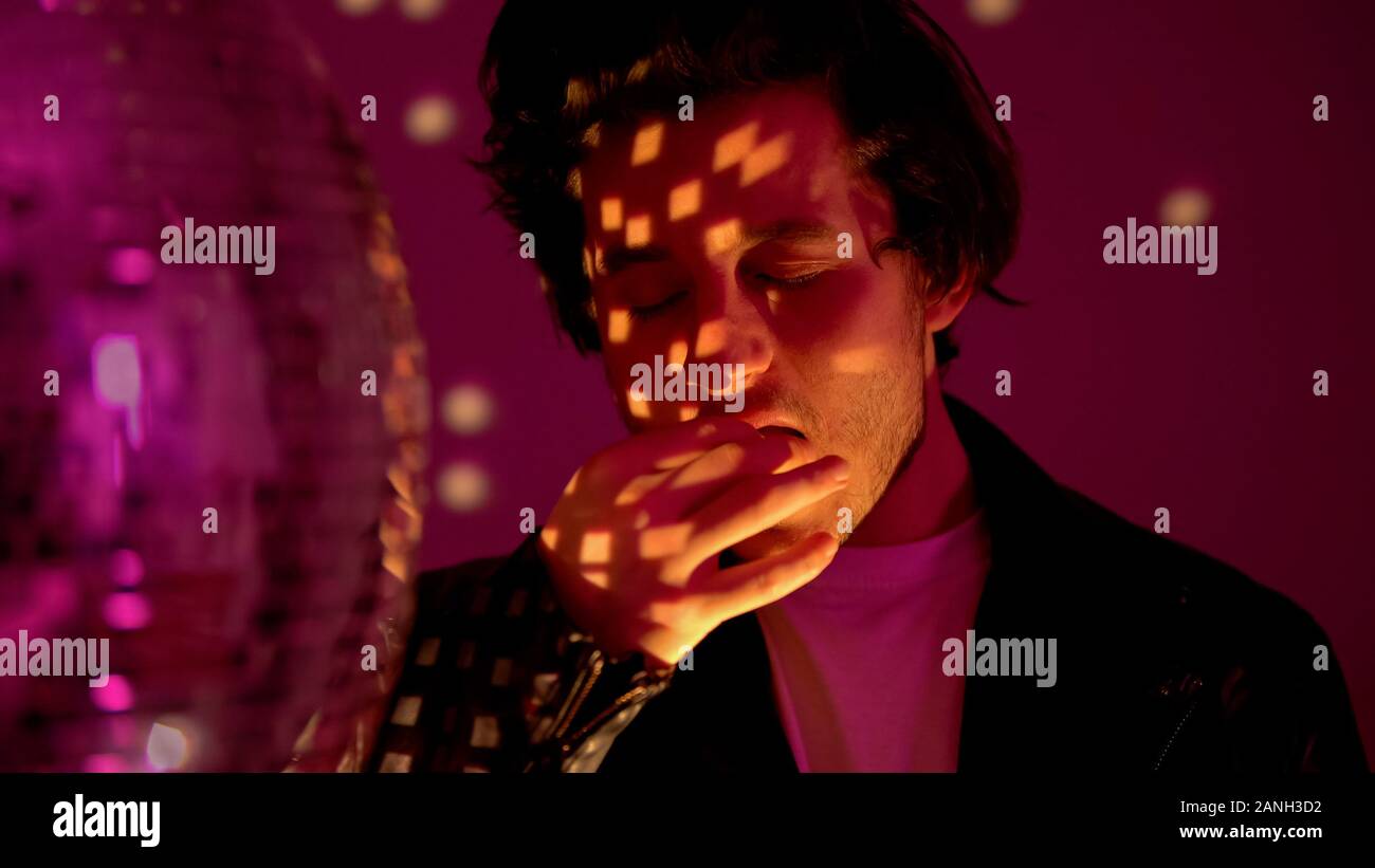 Relaxed man taking ecstasy pill near disco ball in club, party atmosphere Stock Photo