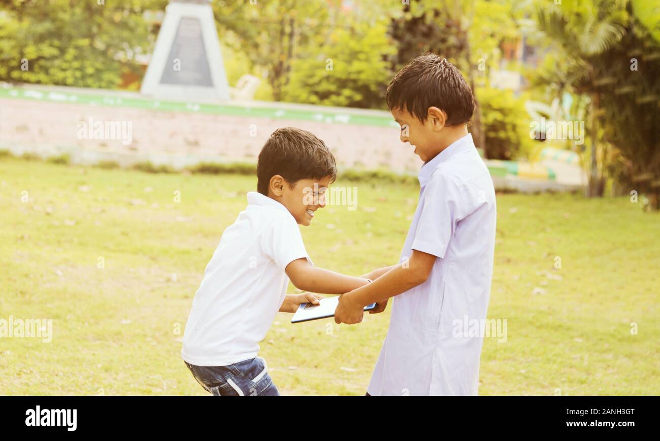 Two kids fighting for tablet at park outdoor - Liite boy trying to grab a tablet from her friend or brother - Concept of children's addiction Stock Photo