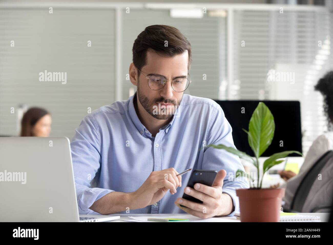 Serious male office manager work in coworking space using smartphone analyzing online market trends, focused man worker reading financial news or brow Stock Photo