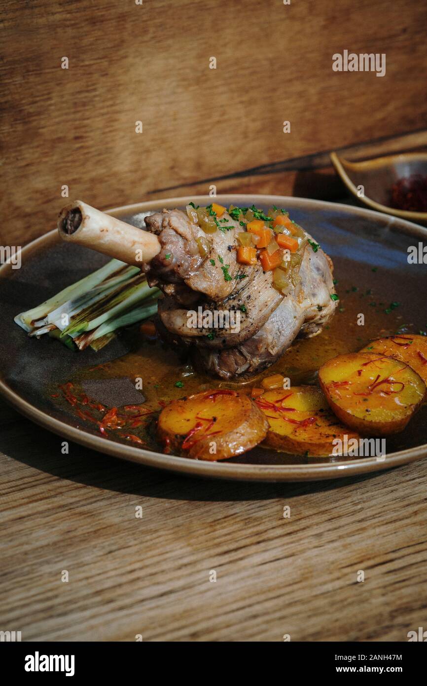 Roast dinner. Main course of roasted Lamb shank with saffron potatoes and leek, Wooden background Stock Photo