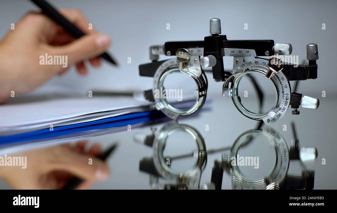 Doctor writing eyeglass prescription, vision check with optical trial frame Stock Photo