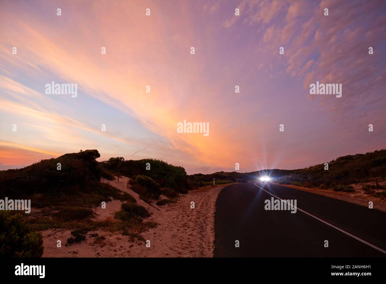 Car driving at sunset on scenic road with glowing high beam lights