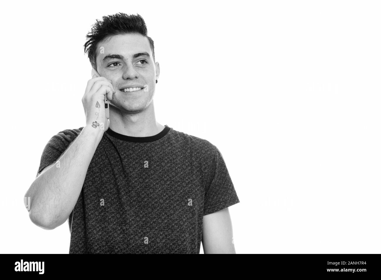 Studio shot of happy young man smiling while talking on mobile phone and thinking Stock Photo