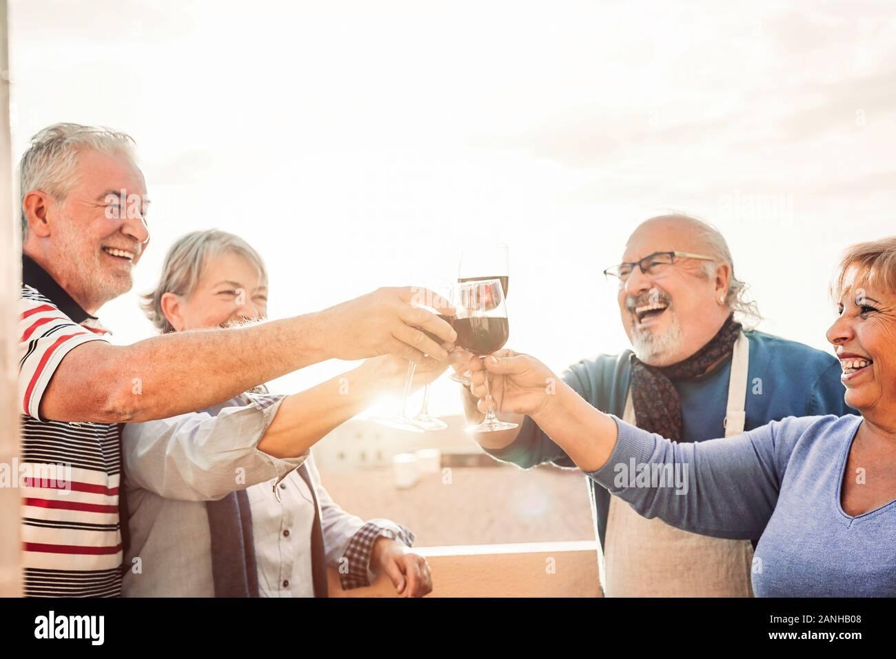 Happy seniors friends drinking red wine on terrace sunset - Pensioners people having fun enjoying time together outdoor Stock Photo