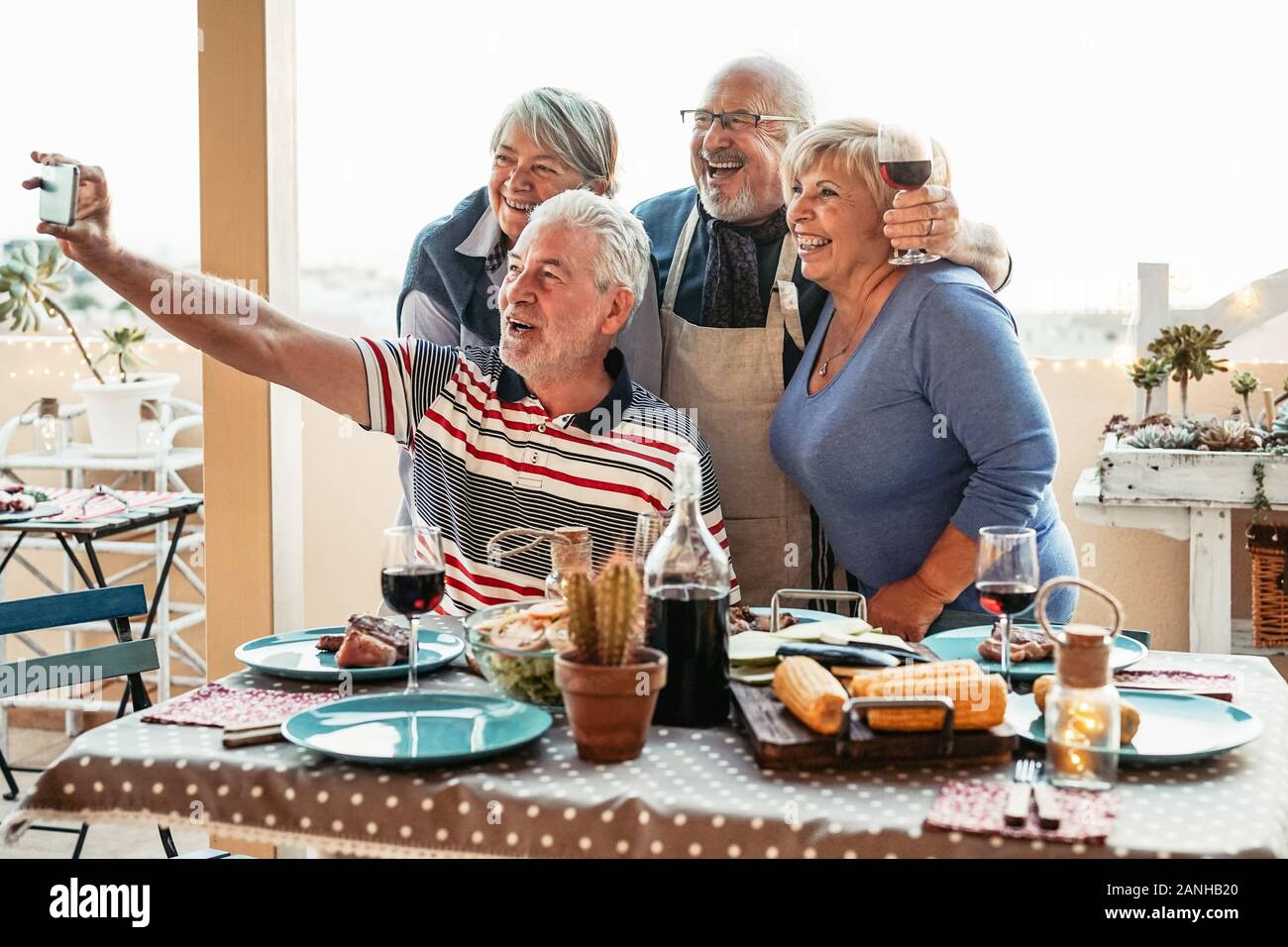 Happy seniors friends taking selfie with mobile smartphone camera at dinner on terrace - Retired people having fun eating and drinking red wine Stock Photo